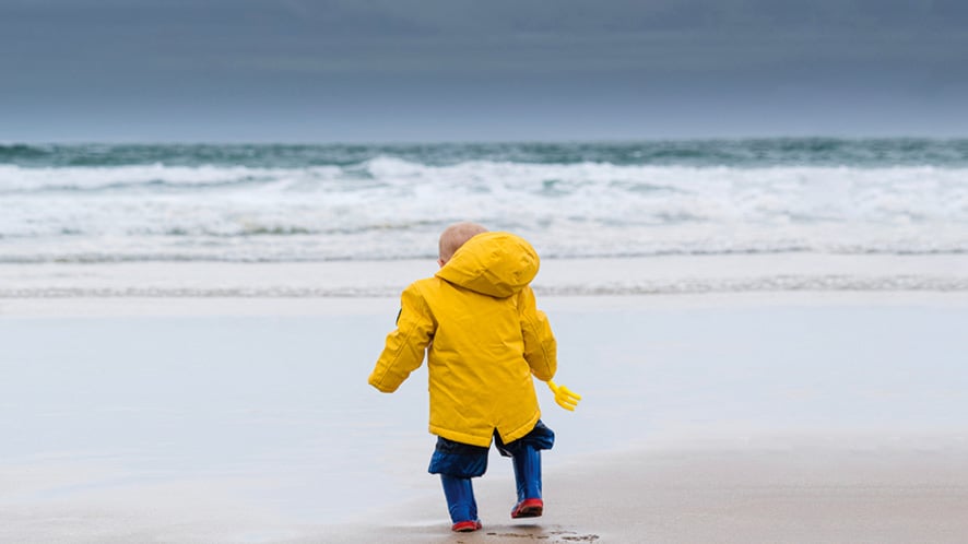 Young child wearing a yellow coat on a wintery beach