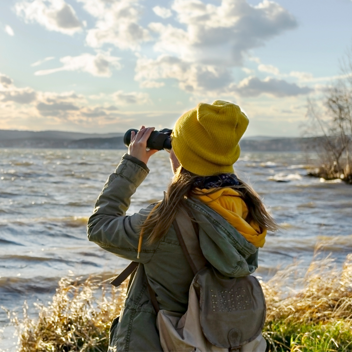 lady with a yellow hat and binoculars looking out at water