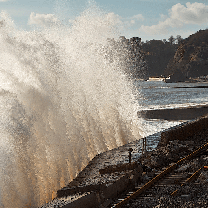 Picture of a storm. A wave can be seen crashing over a railway track