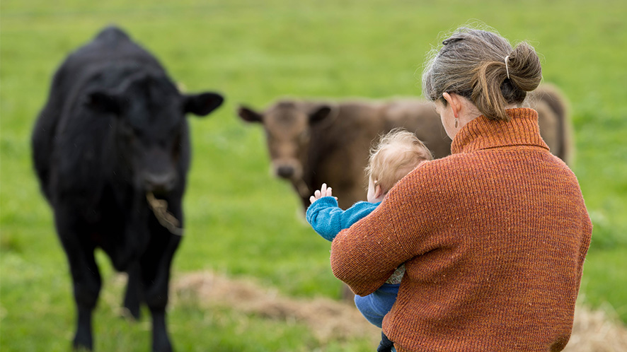 Farmer with her baby looking out at a field of cows